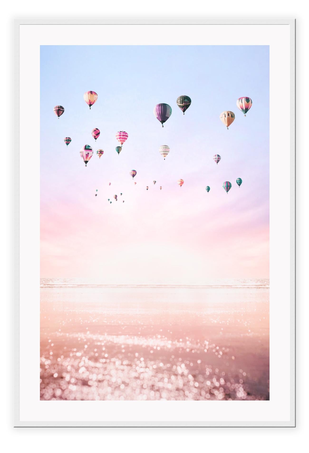 A framed print of multiple hot air balloons floating in a pink and purple sky, with a smooth matte wood finish frame.