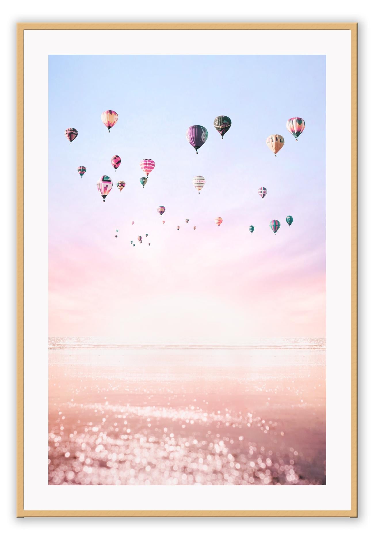A framed print of multiple hot air balloons floating in a pink and purple sky, with a smooth matte wood finish frame.