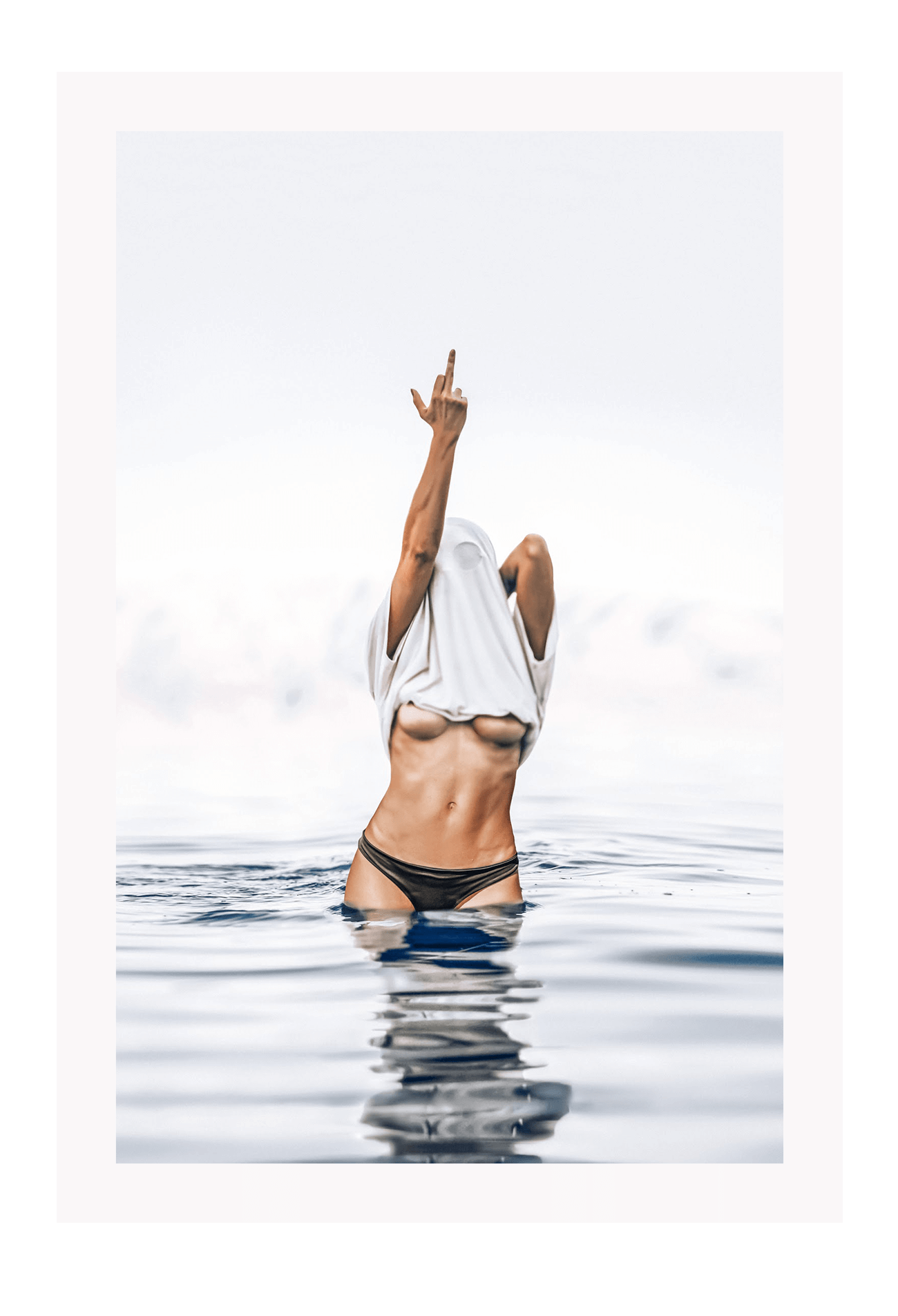 Person in black bikini standing in water with a white towel over their head.