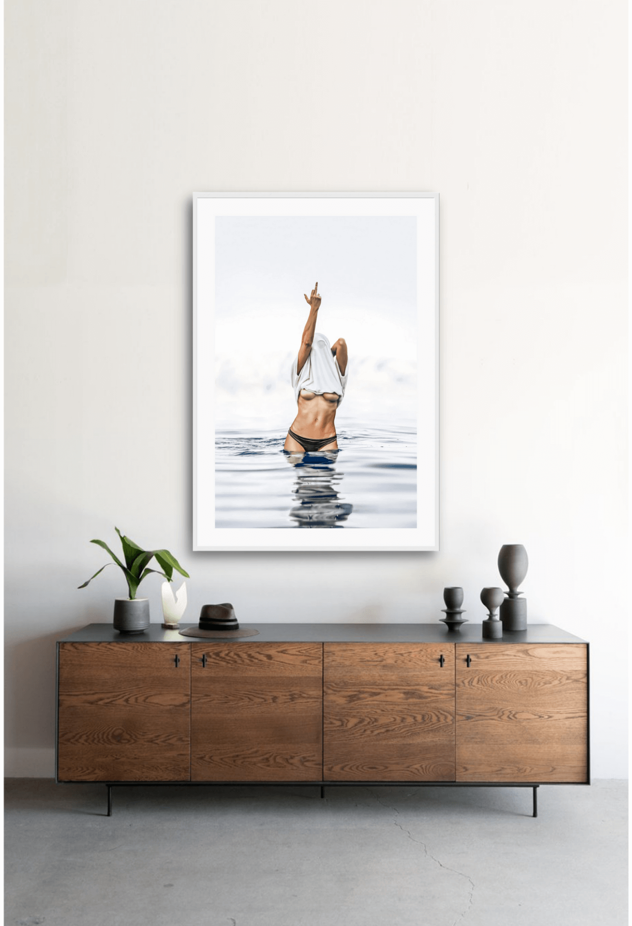 Framed artwork of a person in a swimsuit standing in water above a wooden cabinet.