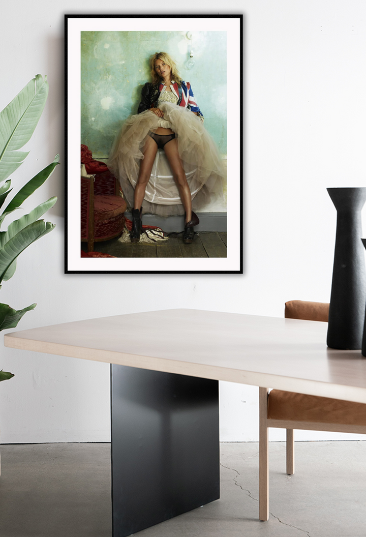 Fashion photography print featuring kate moss in a union jack jacket and hoop skirt lifing it up on a green wall background. Hanging on white wall in office setting.