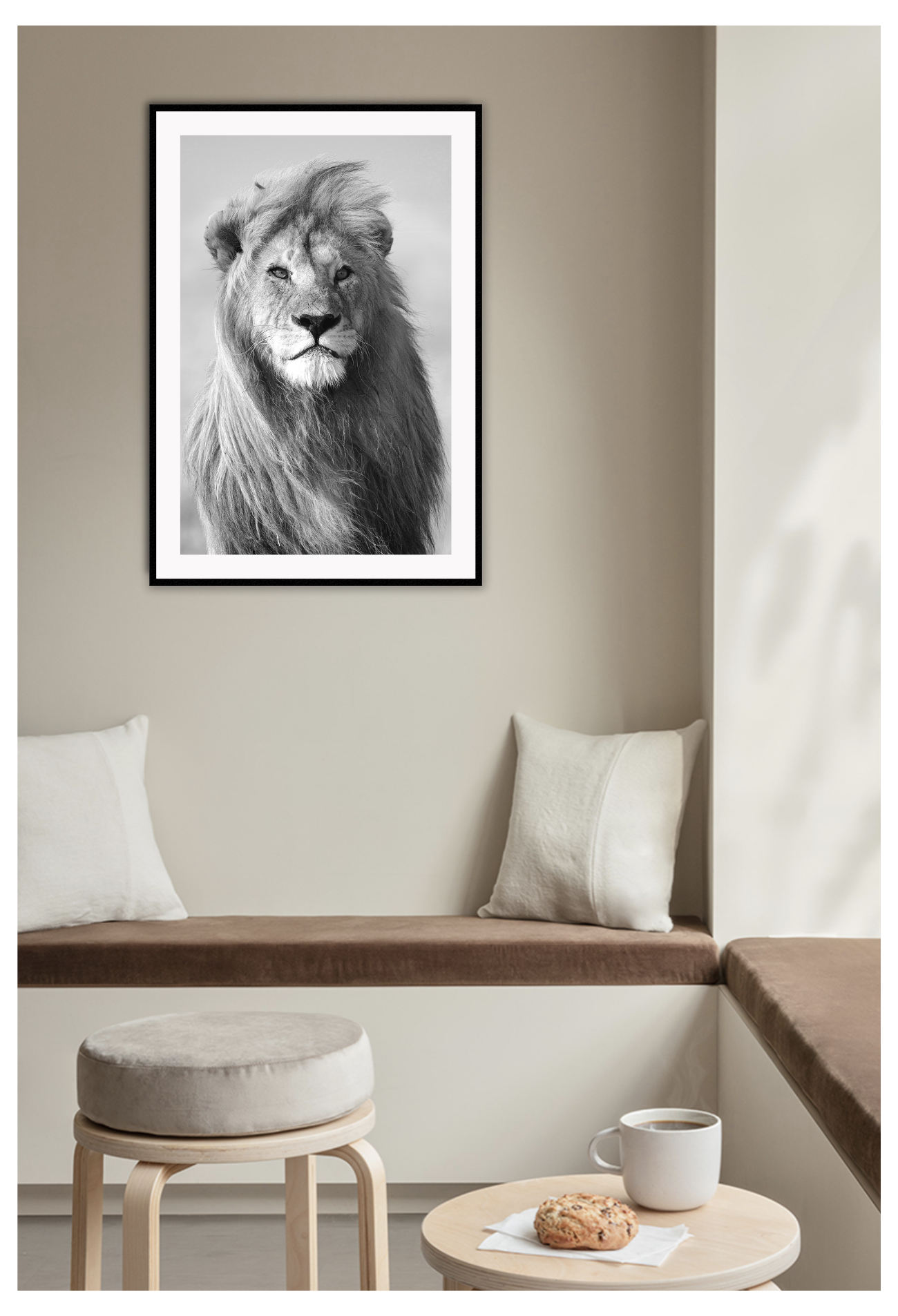 Black and white framed print of a lion, hung on a beige wall above brown seat with white cushions.