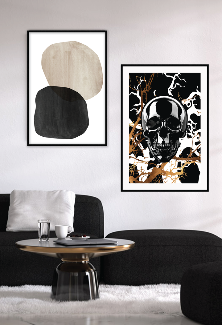 A framed art print featuring a stylized, black skull with gold and black branches in the background, set in a matte black frame. Hung on a white wall above a black lounge.
