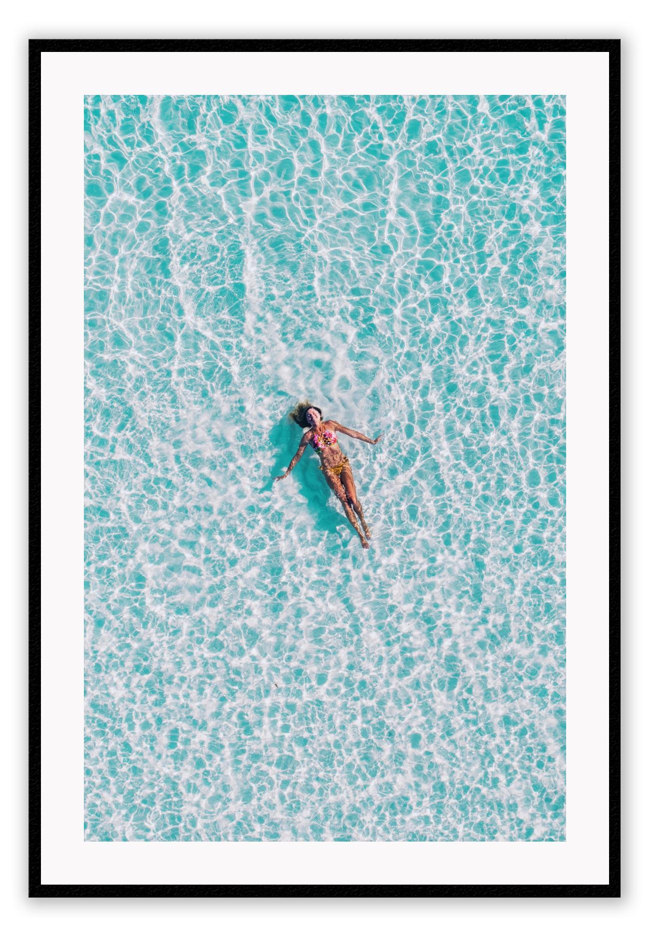 A framed print depicting a person swimming in a turquoise ocean, with a high quality custom frame.