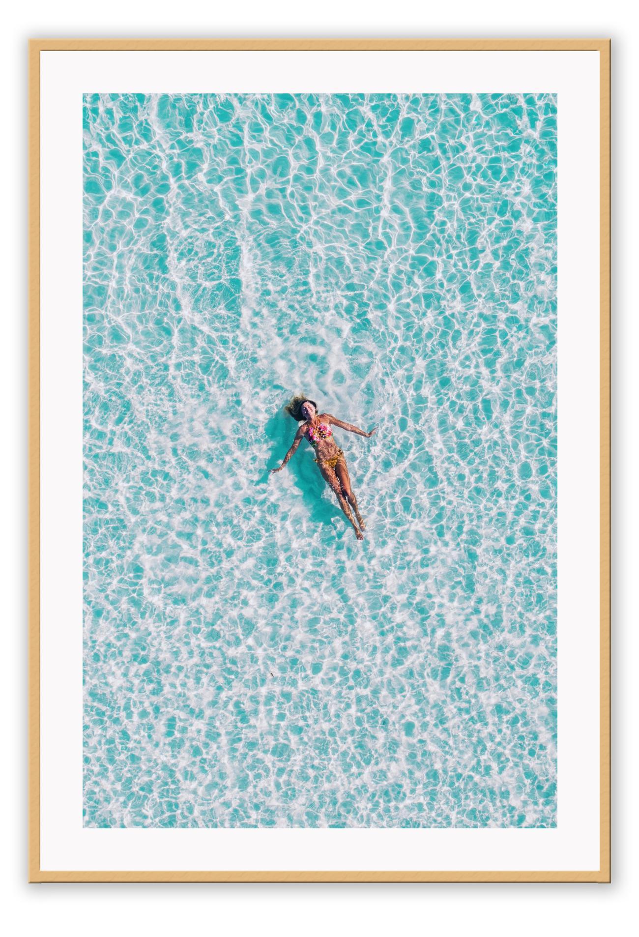 A framed print depicting a person swimming in a turquoise ocean, with a high quality custom frame.