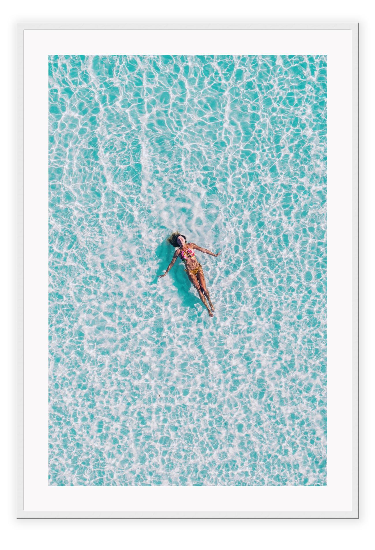 A framed print depicting a person swimming in a turquoise ocean, with a high quality custom frame.