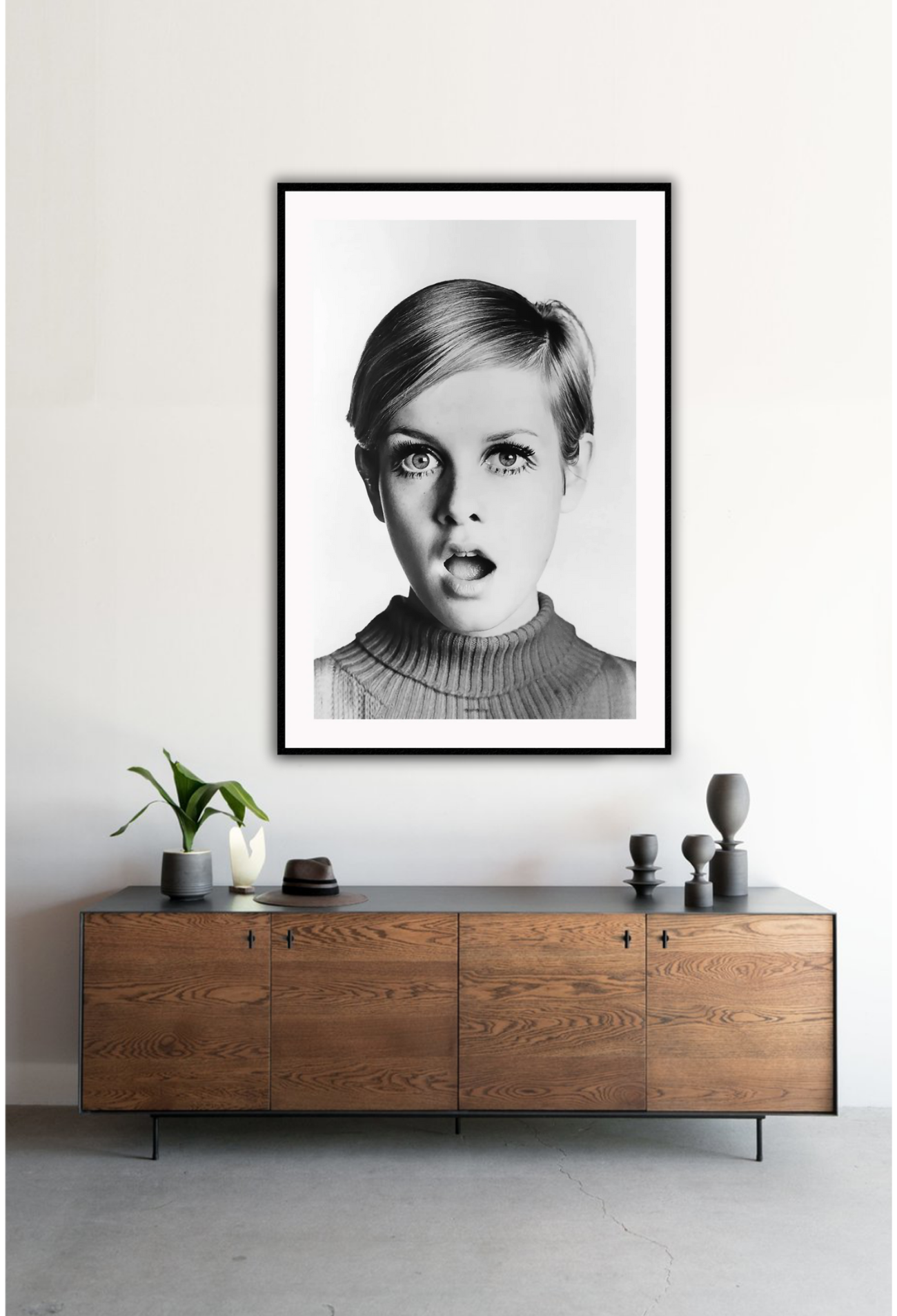 A framed black and white portrait of Twiggy looking directly at the camera with a surprised expression, mounted in a high quality custom made frame. Mounted on a white wall above a timber cabinet.