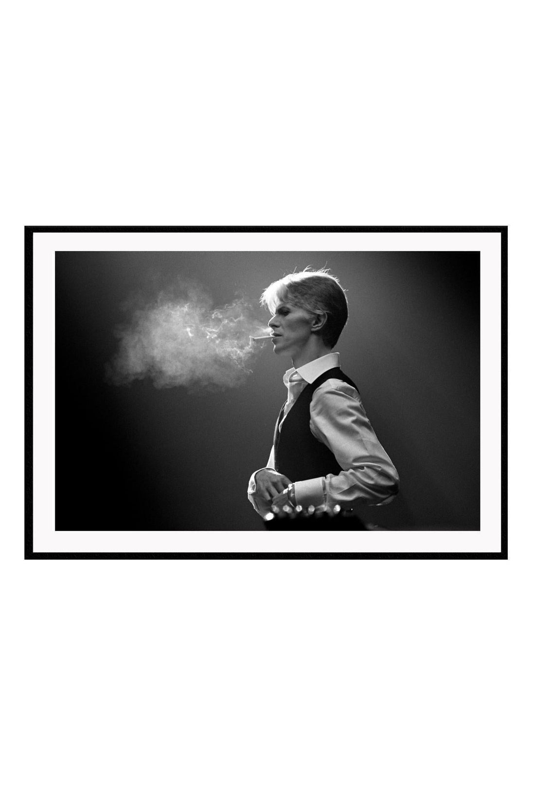 A framed black and white photograph of David Bowie, with smoke surrounding him, mounted in a frame with a matte wood finish.