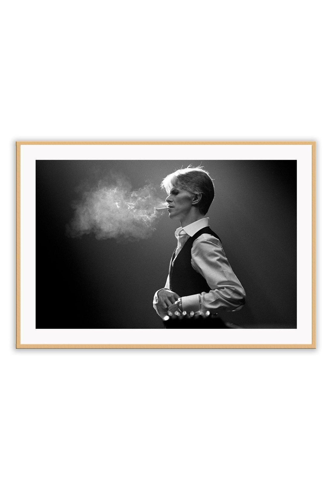 A framed black and white photograph of David Bowie, with smoke surrounding him, mounted in a frame with a matte wood finish.