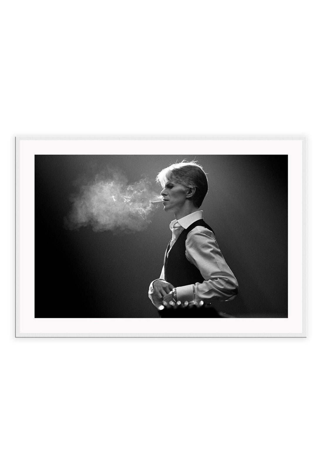 A framed black and white photograph of David Bowie, with smoke surrounding him, mounted in a frame with a matte wood finish.