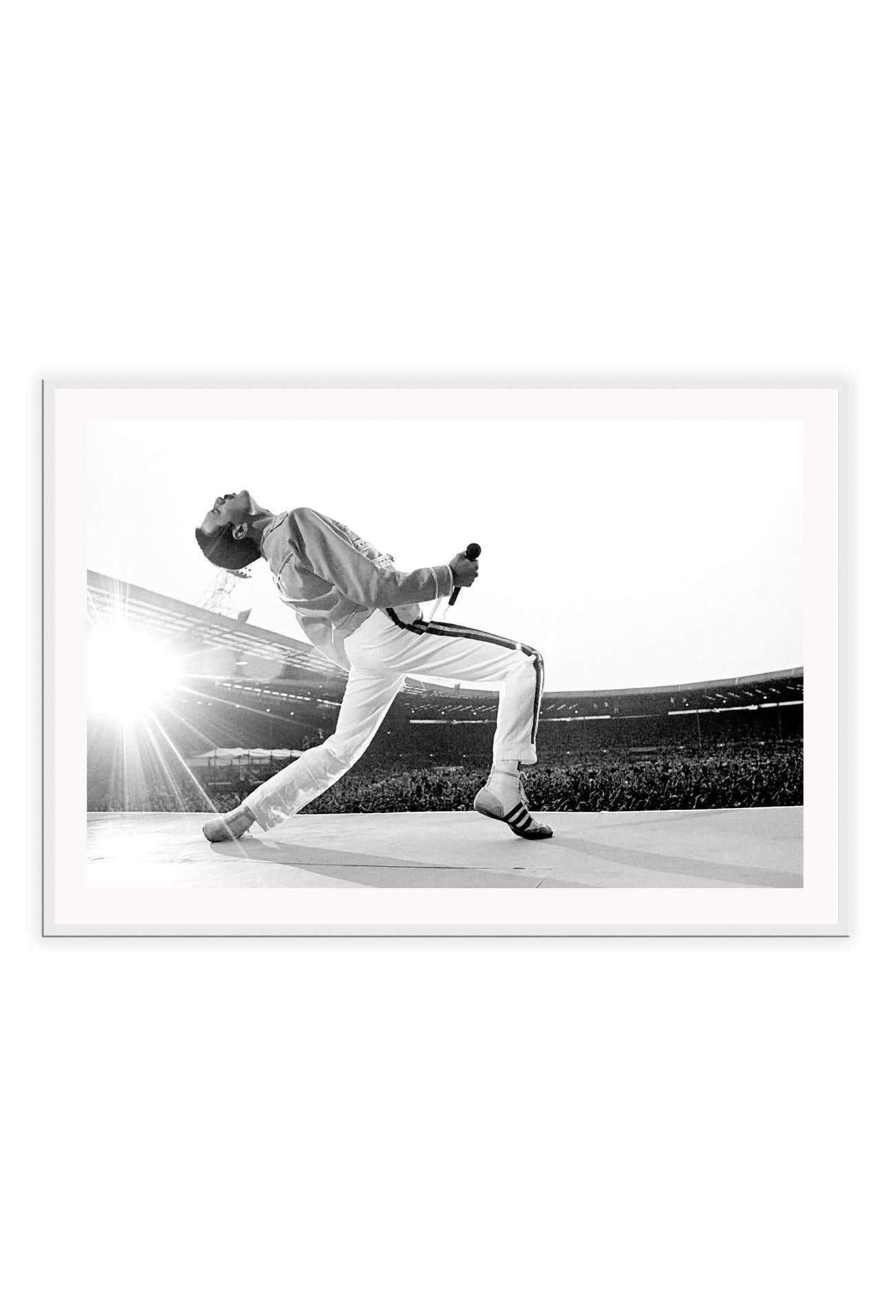 A framed black and white photograph of Freddie Mercury in a dynamic pose, mounted in a matte black frame.