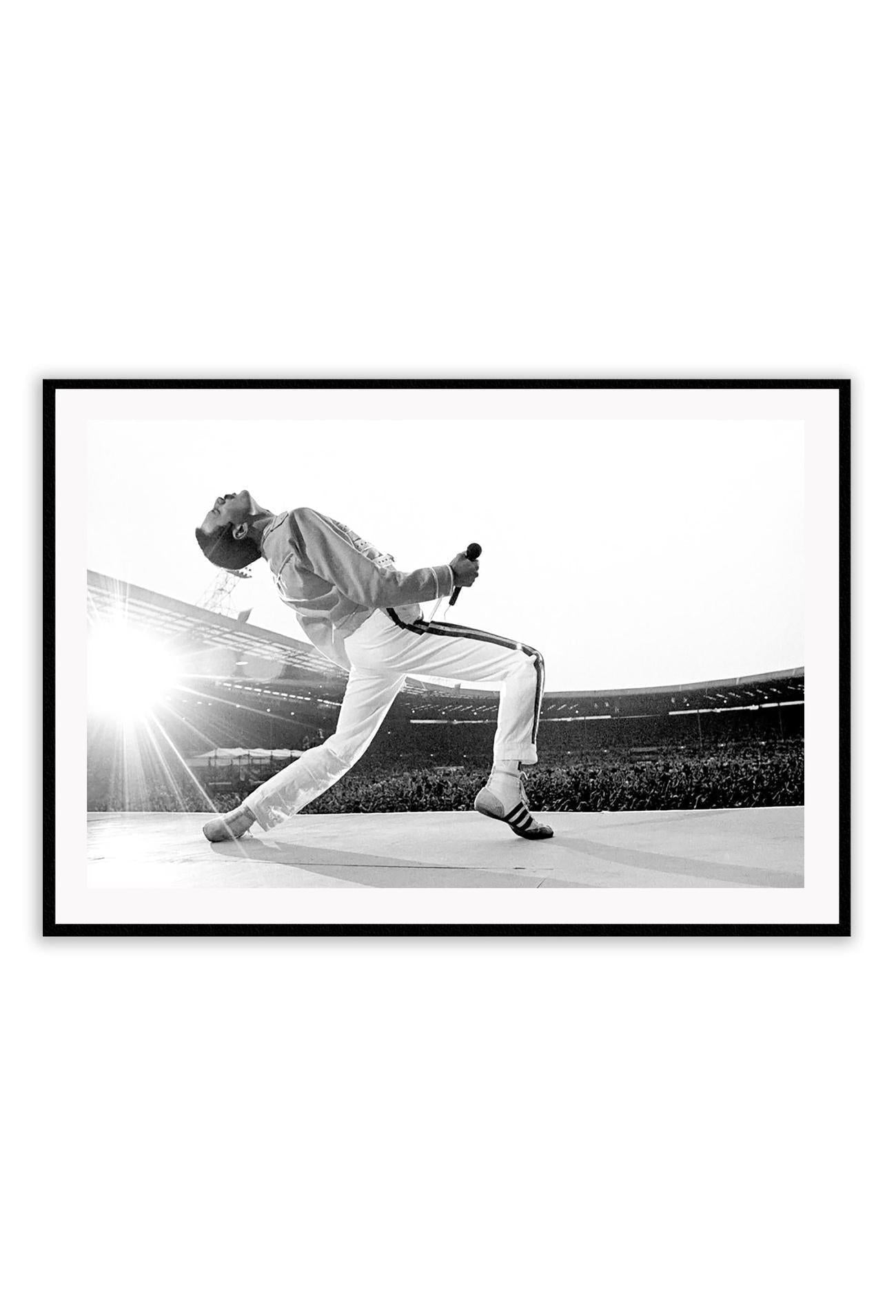A framed black and white photograph of Freddie Mercury in a dynamic pose, mounted in a matte black frame.