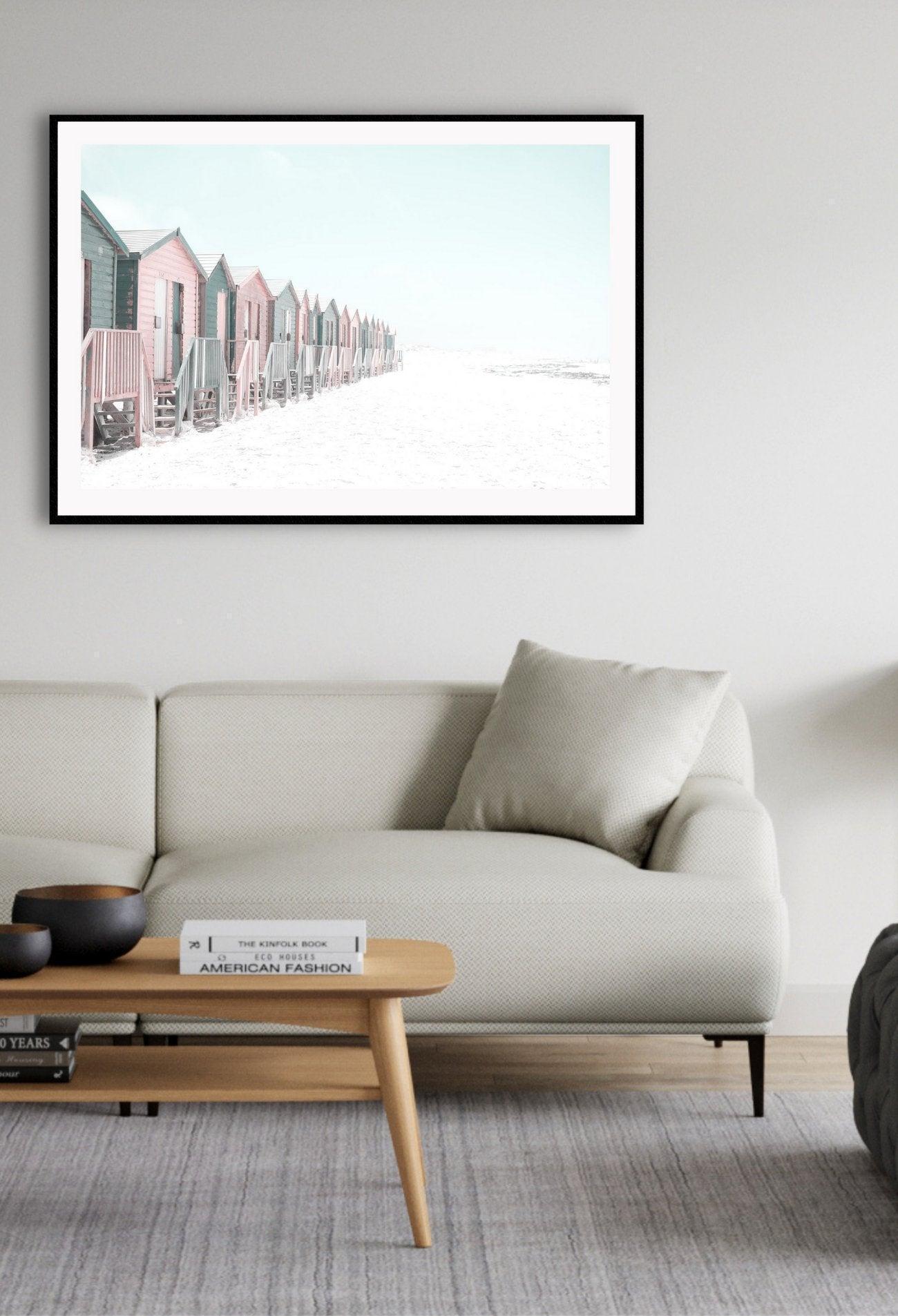 Pink and grey beach houses on sand lined in a row, blue sky.