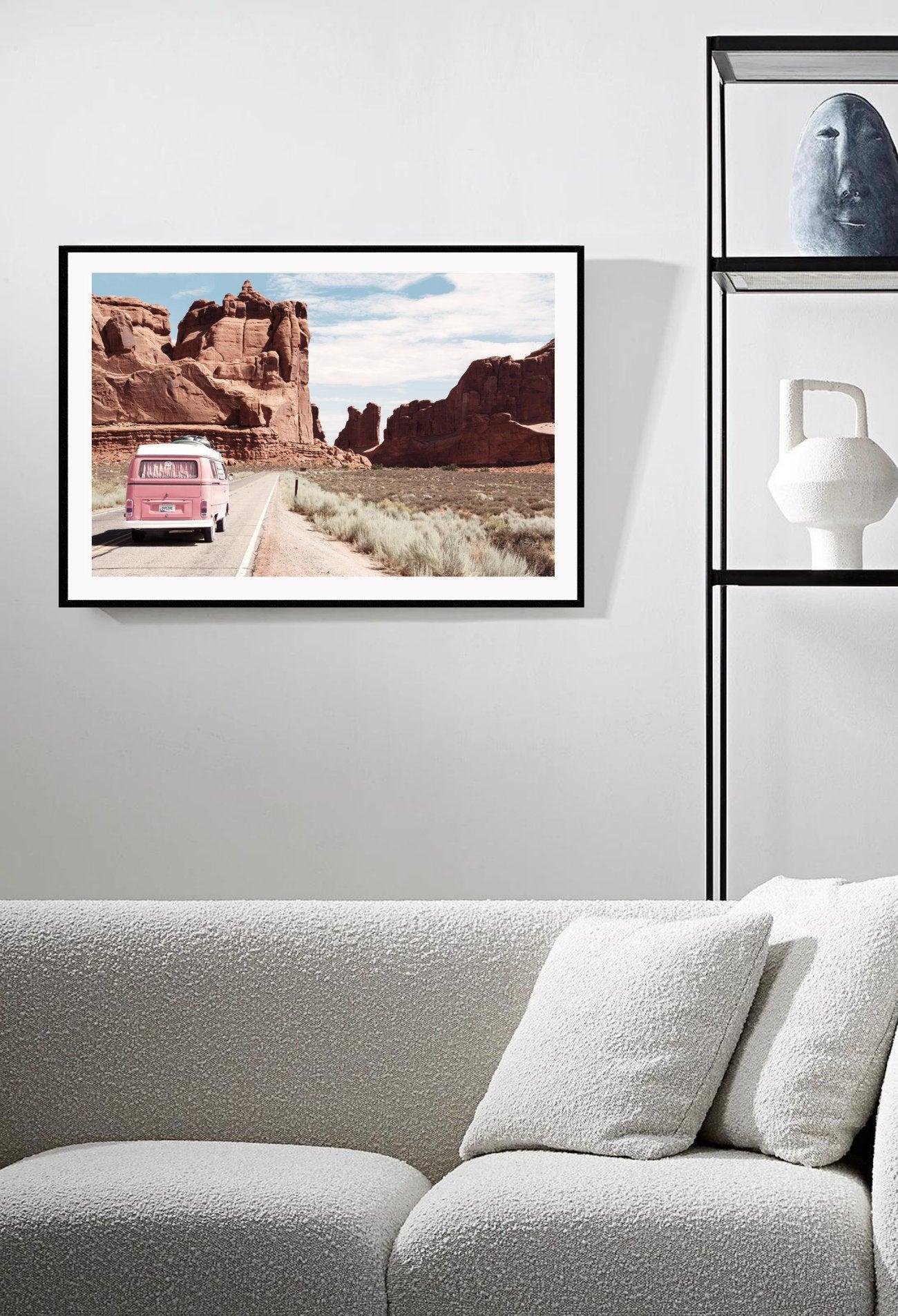 Pink van driving through desert road and grassland with large cliffs in background